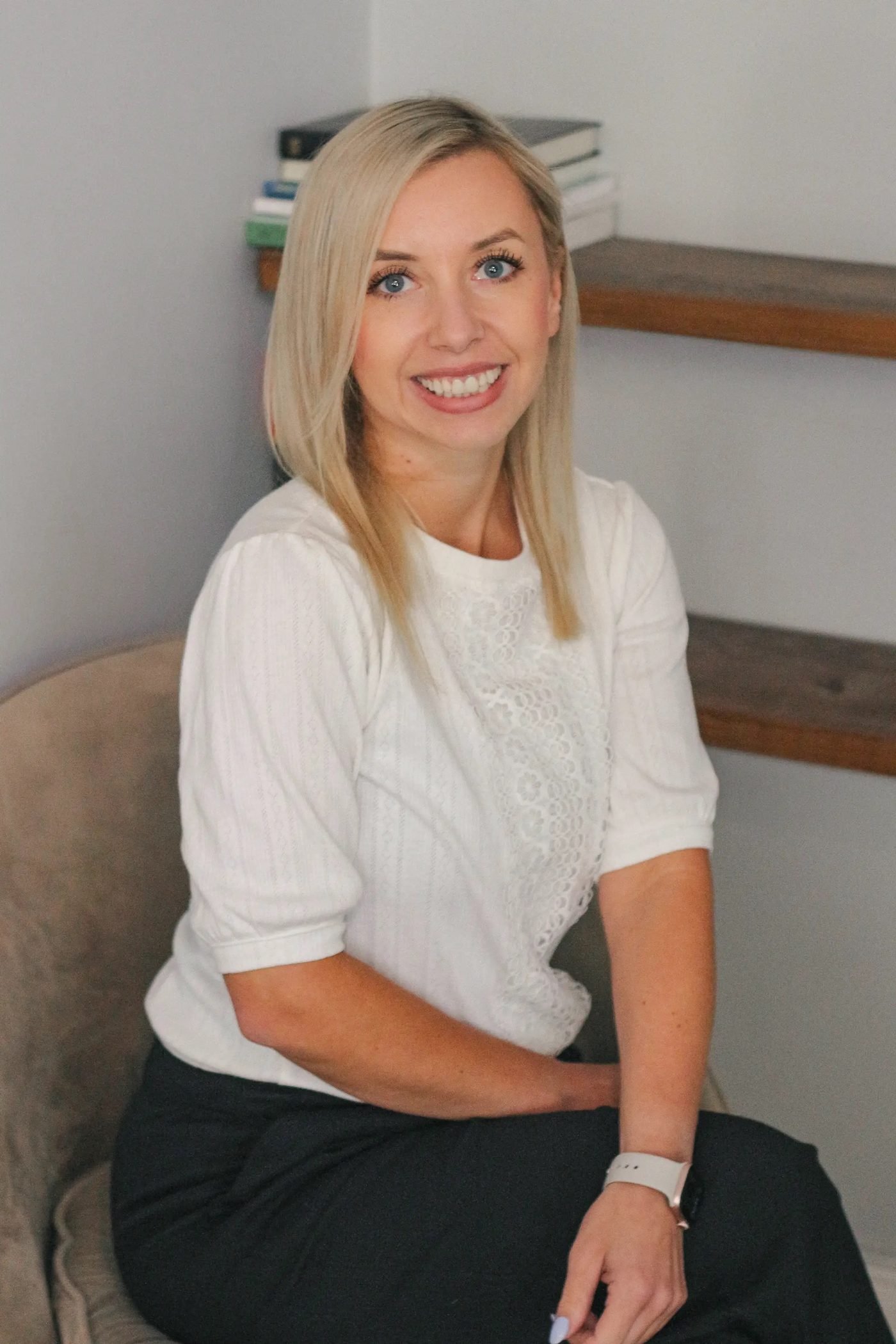 Kat, a CBT therapist and Accredited EMDR practitioner, seated in a chair beside a shelf of books.